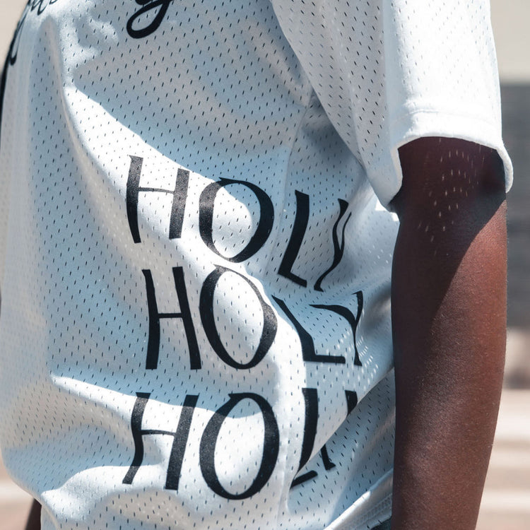Person wearing a white sports jersey with 'HOLY' printed on it, standing outdoors.